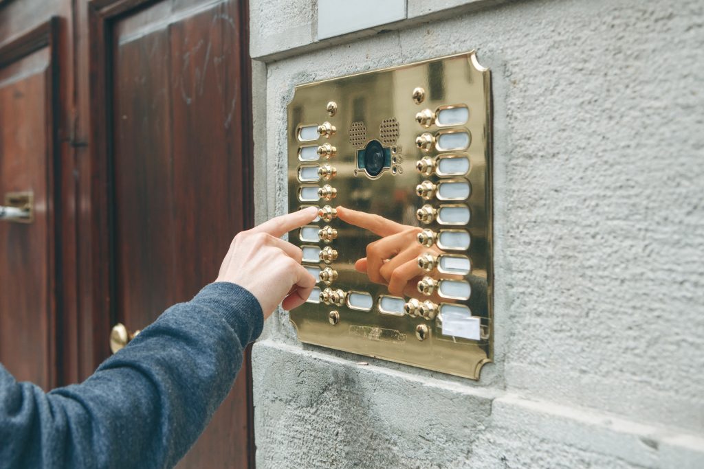 A male hand presses a hardwired doorphone button for access inside