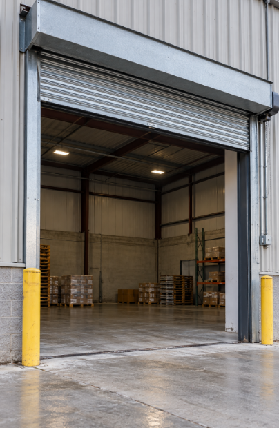 Warehouse loading opening with a steel gate raised to the top and stacked pallets on the concrete floor inside